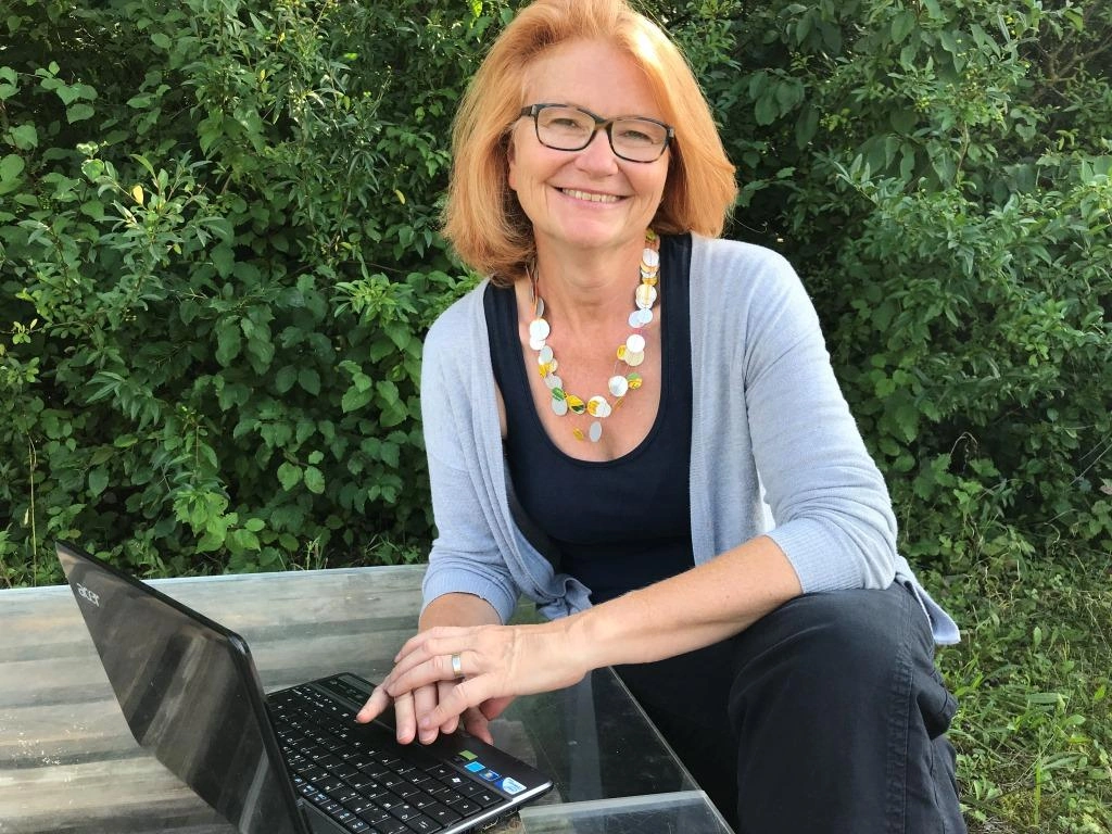 Maria Richter von Mindful-Business vor einem Laptop, kurze offene Haare und Brille, sie lächelt